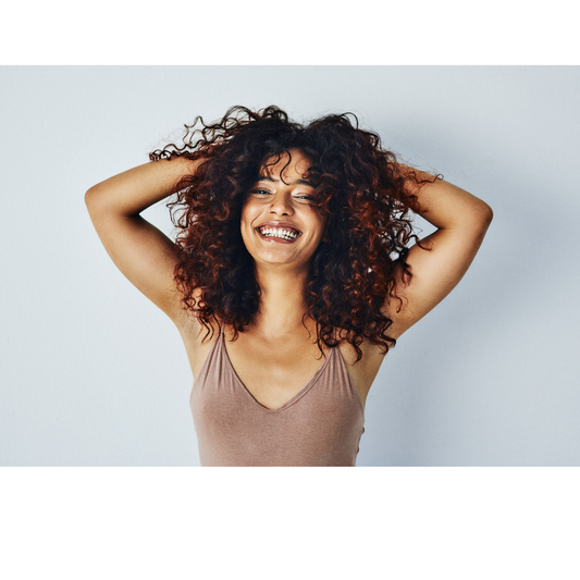 Woman with healthy, voluminous curly hair running her hands through it and smiling